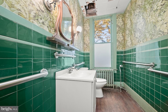 bathroom with radiator heating unit, wood-type flooring, toilet, vanity, and tile walls