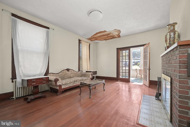 living area featuring french doors, a brick fireplace, a textured ceiling, wood-type flooring, and radiator heating unit