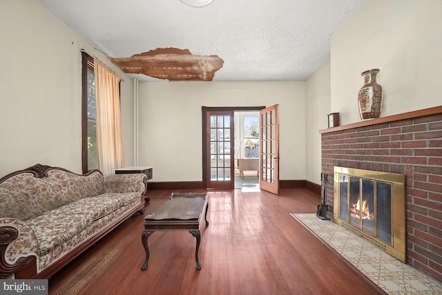 living room featuring a textured ceiling, hardwood / wood-style floors, french doors, and a brick fireplace