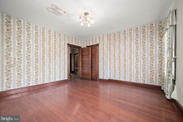 spare room featuring a chandelier and dark wood-type flooring