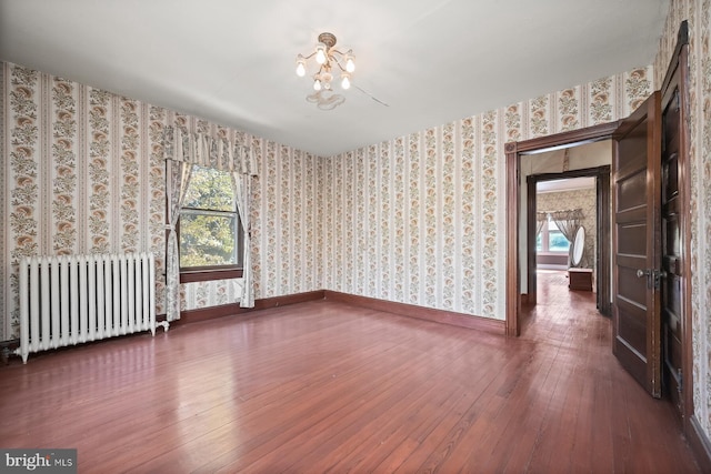 spare room with a notable chandelier, dark hardwood / wood-style flooring, radiator heating unit, and a wealth of natural light