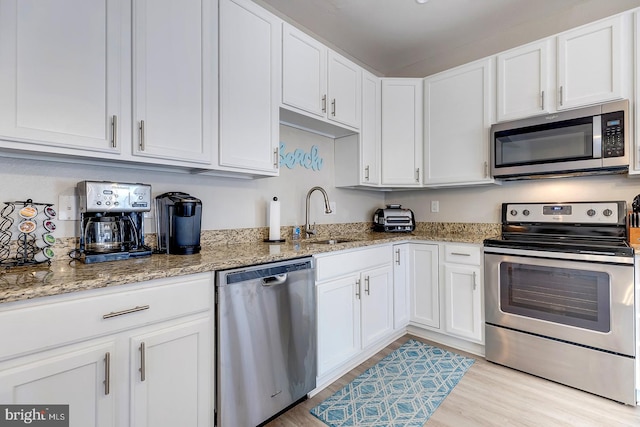 kitchen with white cabinets, appliances with stainless steel finishes, light stone countertops, light hardwood / wood-style floors, and sink