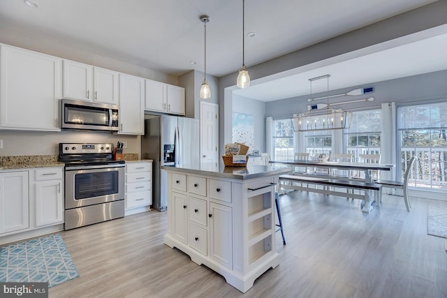 kitchen with pendant lighting, white cabinets, stainless steel appliances, and light hardwood / wood-style floors