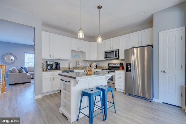 kitchen featuring a kitchen breakfast bar, white cabinets, stainless steel appliances, and decorative light fixtures