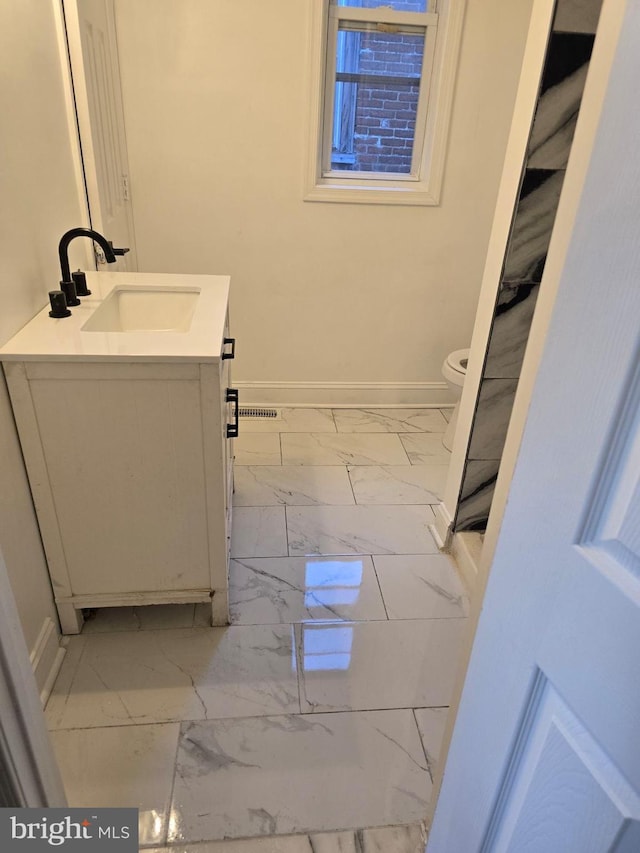 bathroom with toilet, marble finish floor, vanity, and baseboards