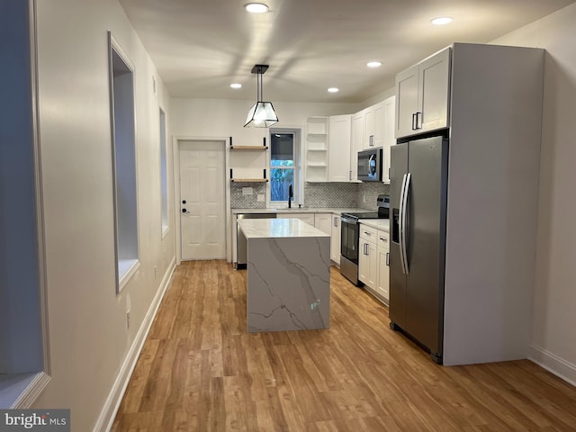 kitchen with white cabinets, stainless steel appliances, pendant lighting, light hardwood / wood-style floors, and a center island