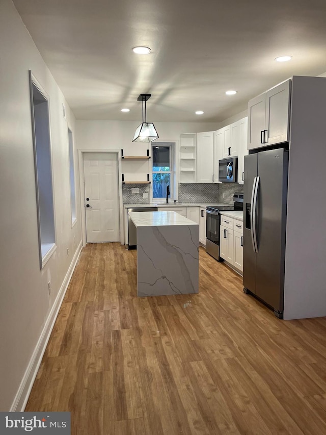 kitchen featuring light wood finished floors, open shelves, hanging light fixtures, appliances with stainless steel finishes, and white cabinetry