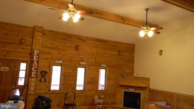 unfurnished living room with a large fireplace, beamed ceiling, wooden walls, and ceiling fan