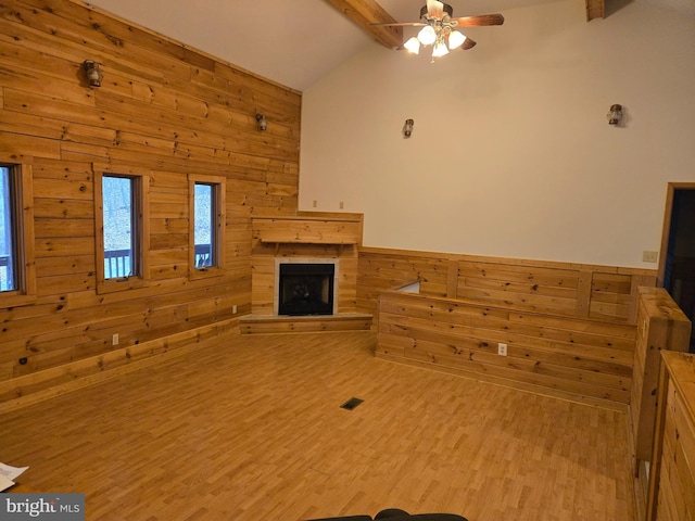 unfurnished living room featuring a fireplace with raised hearth, wooden walls, lofted ceiling with beams, and ceiling fan