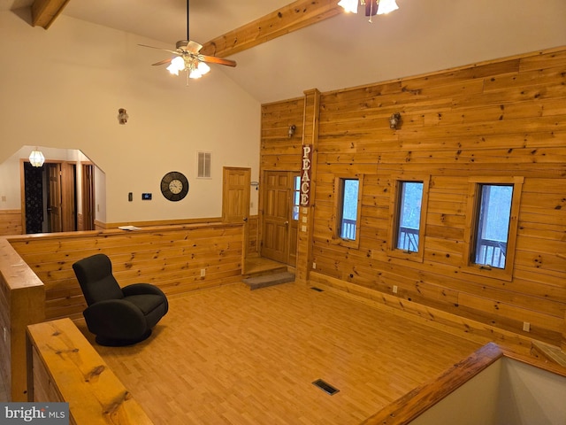 unfurnished living room with lofted ceiling with beams, a wainscoted wall, visible vents, ceiling fan, and wooden walls