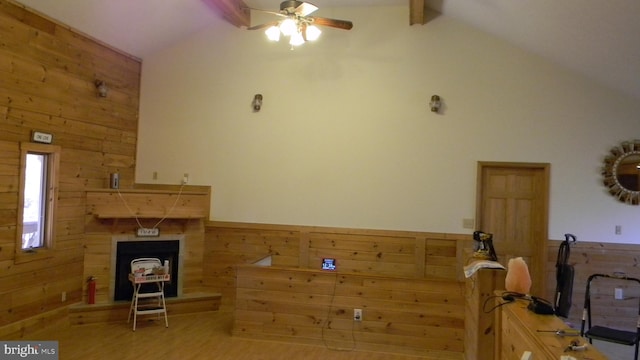 unfurnished living room featuring high vaulted ceiling, wood walls, light hardwood / wood-style floors, beamed ceiling, and ceiling fan