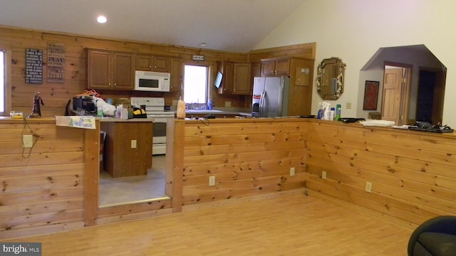 kitchen featuring light wood-type flooring, white appliances, wood walls, a breakfast bar, and kitchen peninsula