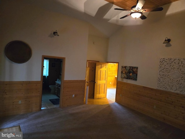 unfurnished bedroom with wood walls, ensuite bathroom, high vaulted ceiling, carpet flooring, and wainscoting