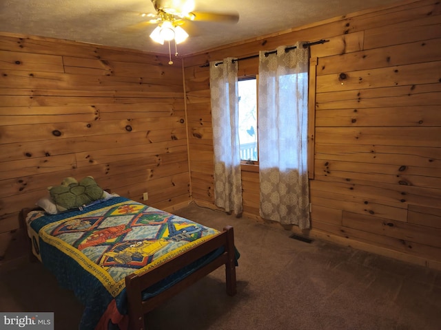 bedroom with carpet, wood walls, a ceiling fan, and visible vents