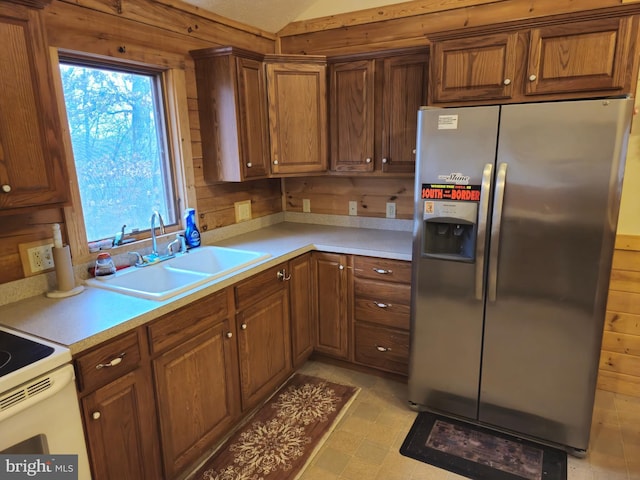 kitchen with light countertops, a sink, wood walls, and stainless steel refrigerator with ice dispenser
