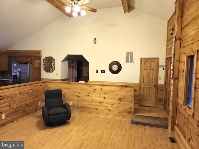 sitting room featuring visible vents, wood walls, and vaulted ceiling with beams