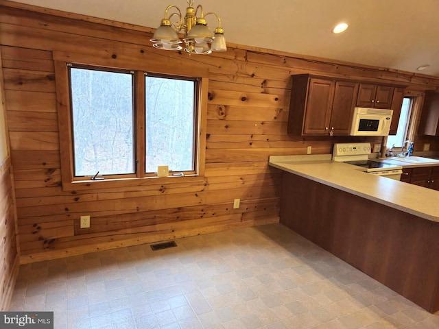 kitchen with wood walls, white appliances, visible vents, light countertops, and a notable chandelier