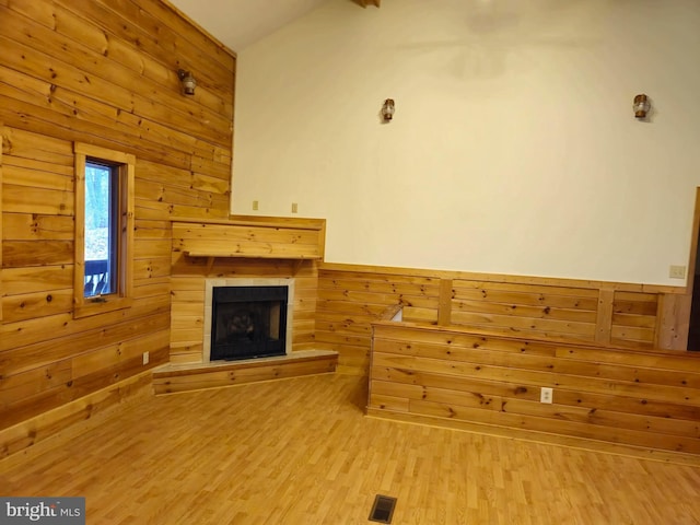 unfurnished living room featuring a tile fireplace, wooden walls, visible vents, and wood finished floors