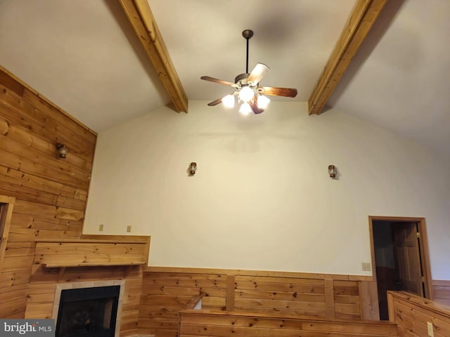 unfurnished living room with wooden walls, a fireplace, a ceiling fan, and vaulted ceiling with beams