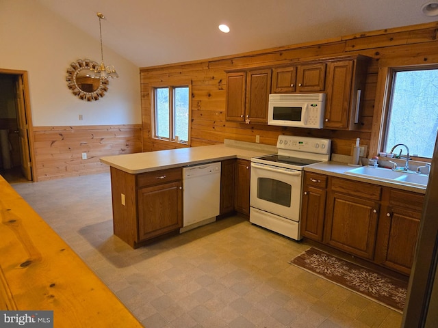 kitchen featuring a peninsula, a sink, light floors, white appliances, and wooden walls