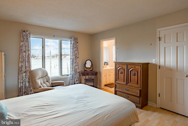 bedroom featuring ensuite bathroom, a water view, a textured ceiling, and light wood-type flooring