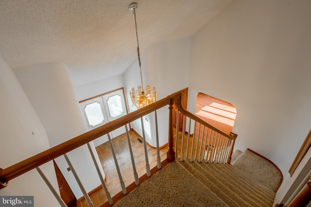 stairs with carpet, a notable chandelier, and a textured ceiling