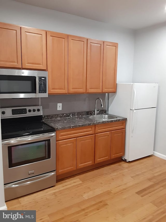 kitchen with appliances with stainless steel finishes, light hardwood / wood-style floors, dark stone counters, and sink