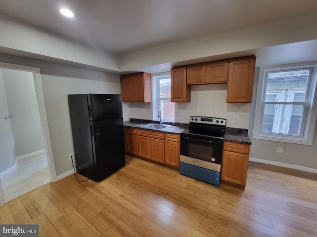 kitchen with electric range oven, tasteful backsplash, sink, black fridge, and light wood-type flooring