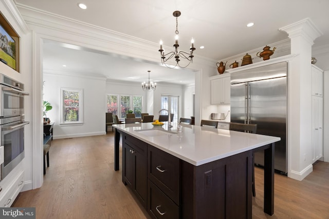 kitchen with a kitchen island with sink, stainless steel appliances, sink, pendant lighting, and light wood-type flooring