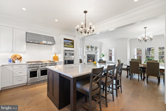 kitchen featuring a kitchen island with sink, wall chimney exhaust hood, stainless steel appliances, hardwood / wood-style floors, and white cabinets