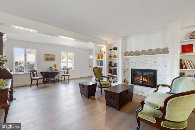 living room featuring built in shelves, wood-type flooring, and a brick fireplace