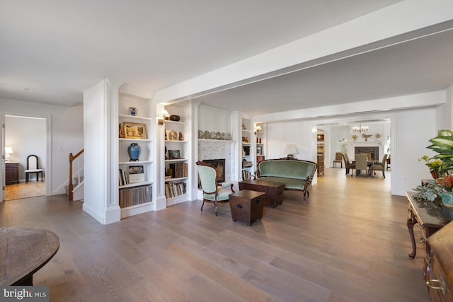 living room featuring a notable chandelier, wood-type flooring, built in features, and a brick fireplace