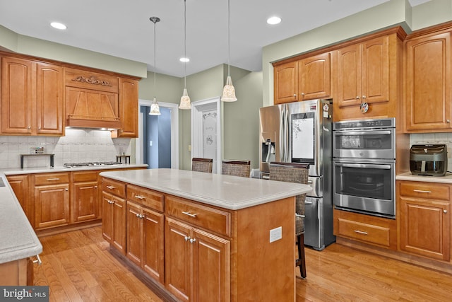 kitchen with decorative backsplash, a kitchen island, hanging light fixtures, appliances with stainless steel finishes, and light hardwood / wood-style floors