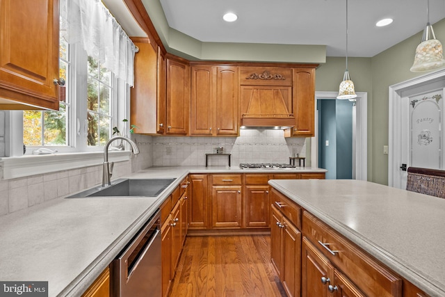 kitchen with sink, light wood-type flooring, stainless steel appliances, decorative light fixtures, and premium range hood