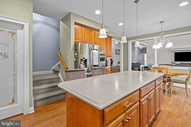 kitchen with hanging light fixtures, a kitchen island, appliances with stainless steel finishes, light wood-type flooring, and a notable chandelier