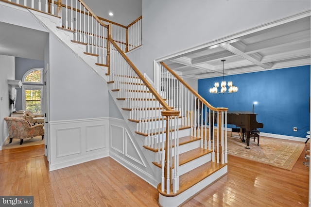 stairs with coffered ceiling, hardwood / wood-style floors, and a chandelier