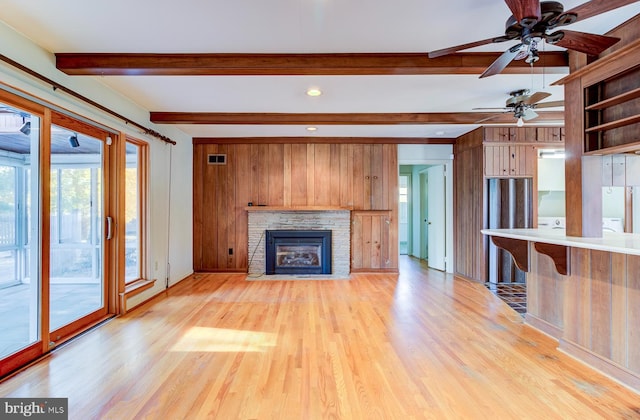 unfurnished living room with a stone fireplace, beamed ceiling, light wood-type flooring, and ceiling fan