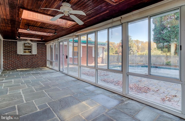 unfurnished sunroom featuring plenty of natural light, wooden ceiling, a skylight, and ceiling fan