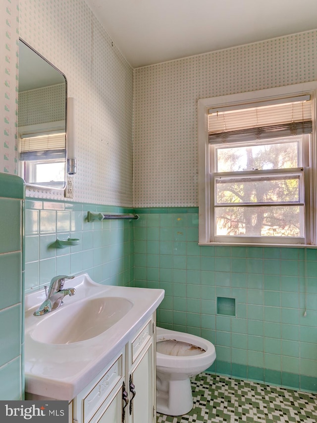 bathroom with toilet, plenty of natural light, vanity, and tile walls