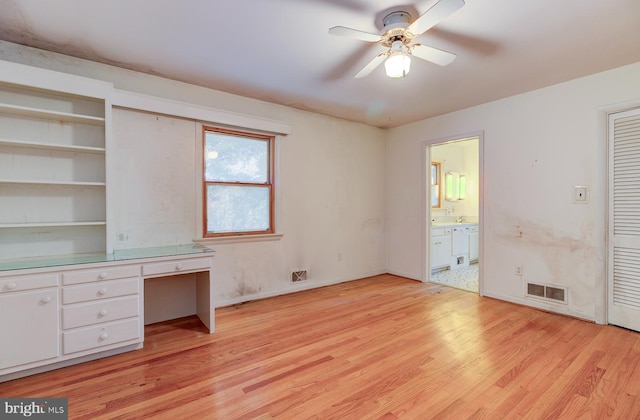 unfurnished bedroom featuring built in desk, ceiling fan, light hardwood / wood-style flooring, and ensuite bathroom