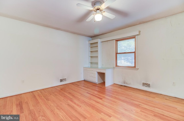 unfurnished room featuring built in desk, ceiling fan, and light hardwood / wood-style flooring