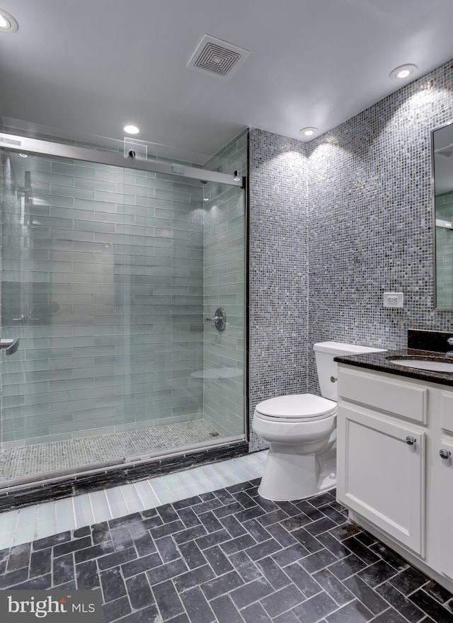 bathroom with tile walls, vanity, toilet, and an enclosed shower