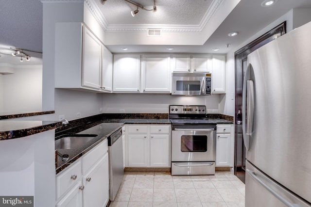 kitchen featuring appliances with stainless steel finishes, white cabinetry, dark stone counters, and ornamental molding