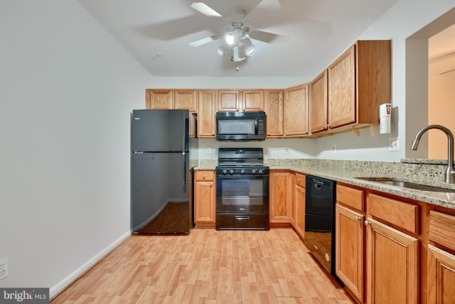 kitchen featuring black appliances, sink, ceiling fan, light stone counters, and light hardwood / wood-style flooring