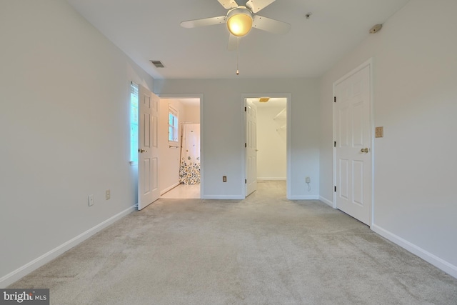 unfurnished bedroom featuring a closet, a spacious closet, light colored carpet, and ceiling fan