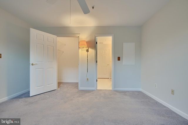 unfurnished bedroom with a closet, ceiling fan, light carpet, and a walk in closet