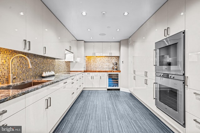 kitchen featuring white cabinetry, sink, beverage cooler, dark stone countertops, and decorative backsplash