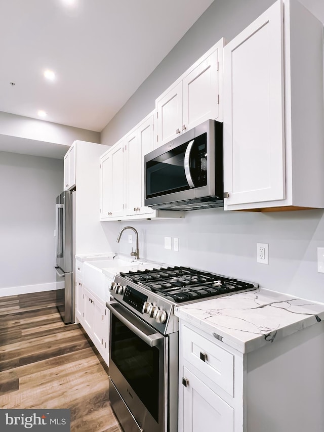 kitchen with white cabinets, light stone counters, stainless steel appliances, and hardwood / wood-style flooring