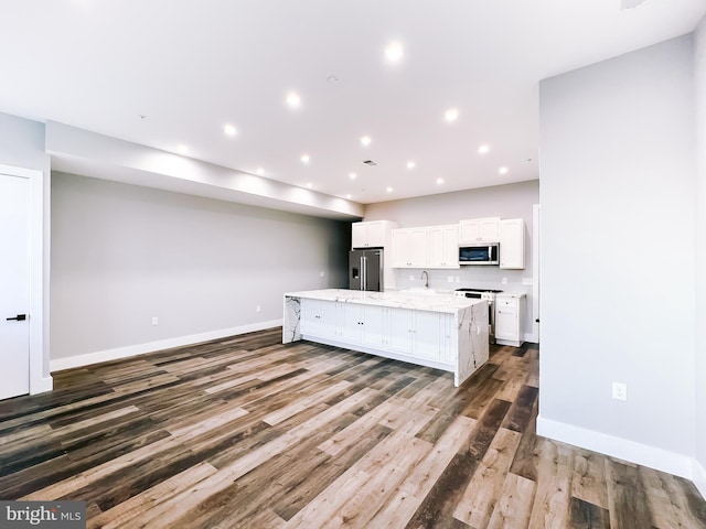 kitchen featuring dark hardwood / wood-style flooring, an island with sink, white cabinetry, light stone countertops, and stainless steel appliances