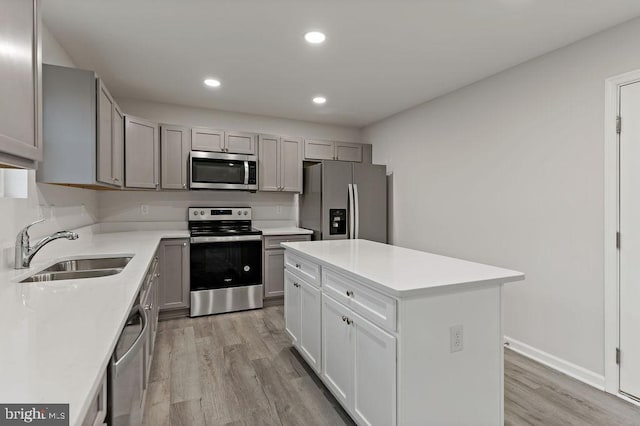 kitchen with gray cabinetry, appliances with stainless steel finishes, sink, light wood-type flooring, and a kitchen island